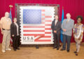 People stand on stage near large stamp display