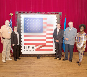 People stand on stage near large stamp display