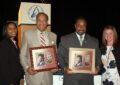 Four people display framed stamp artwork