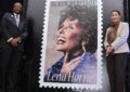 Two people stand on stage next to oversized Lena Horne stamp poster