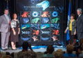 People stand on stage near oversized stamp artwork