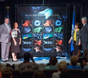 People stand on stage near oversized stamp artwork