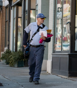 Letter carrier walks down sidewalk