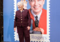 Joanne Rogers stands in front of Mister Rogers stamp poster