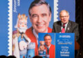 Man speaks at podium near Mister Rogers stamp poster