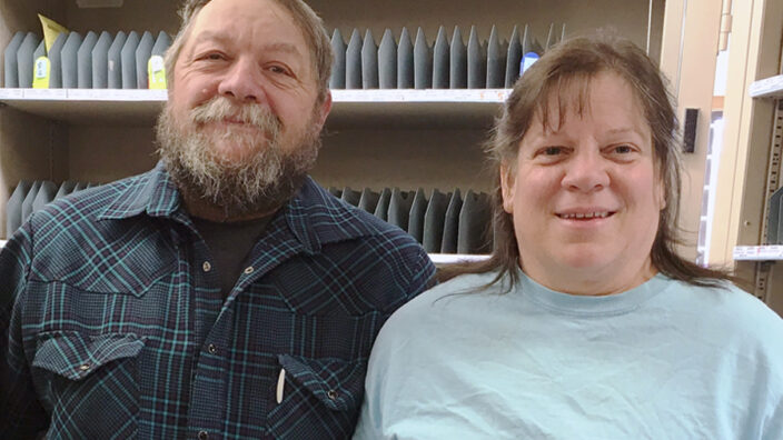 Smiling man, woman stand inside Post Office work room