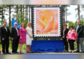 People stand on stage near Peace Rose stamp poster