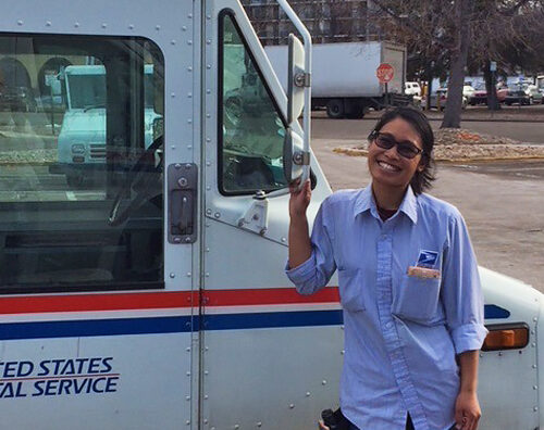 Smiling postal worker stands next to delivery vehicle
