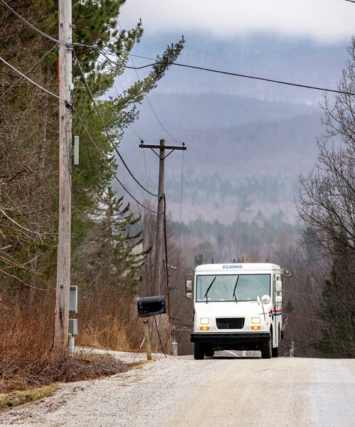 USPS delivery vehicle stops at mailbox on rural road