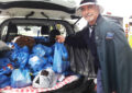 Smiling postal worker adds bag of food to haul in back of delivery vehicle