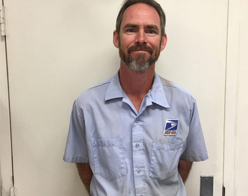 Smiling postal worker stands in front of door