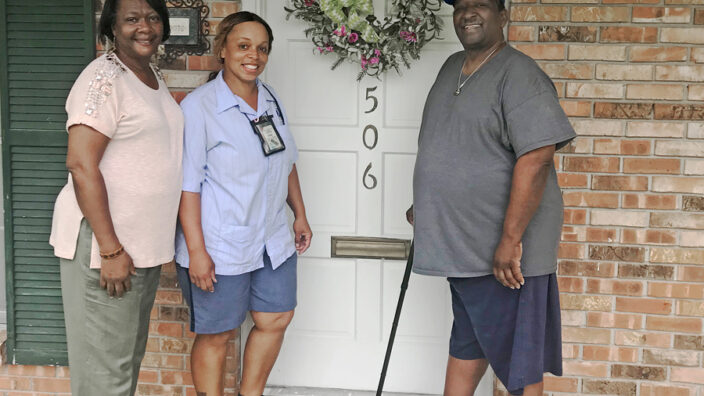 Smiling postal worker stands on front stoop with man, woman