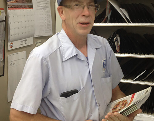 Smiling letter carrier stands in postal workroom