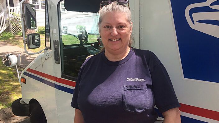 Smiling woman stands next to postal delivery vehicle