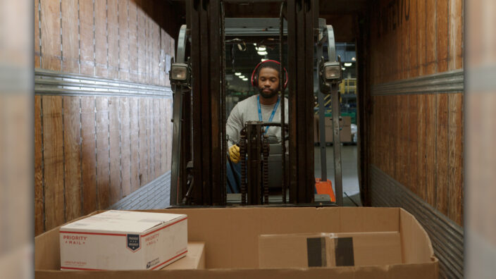 Man wears headphones and operates forklift