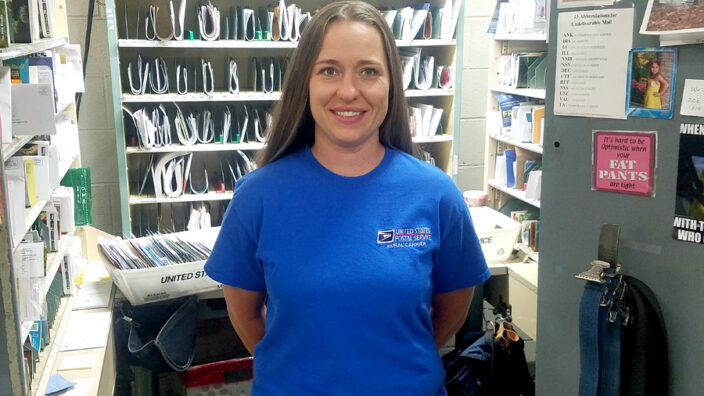 Smiling woman stands in postal workroom