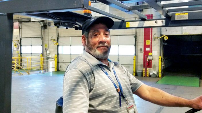 Man sits behind wheel of forklift inside postal plant