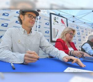 Man, woman sit at table, signing event programs