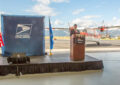 Man stands at podium with airfield behind him