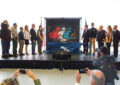 People stand on stage as curtain covering stamp artwork falls