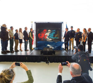 People stand on stage as curtain covering stamp artwork falls