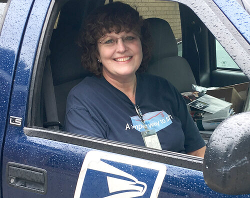 Smiling woman sits inside USPS-branded vehicle