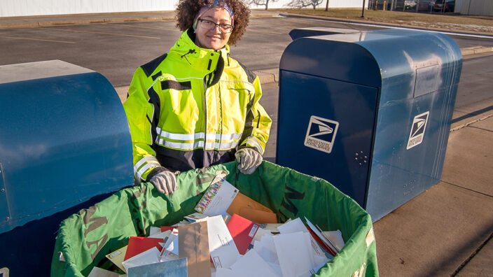Postal worker stands next to bin full of mail