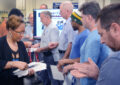 Woman hands envelopes to men who are lined up in postal workroom