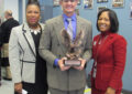 Smiling man displays trophy next to two women