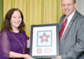 Two smiling people display framed stamp artwork