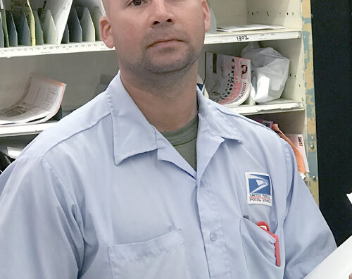 Letter carrier stands in postal workroom