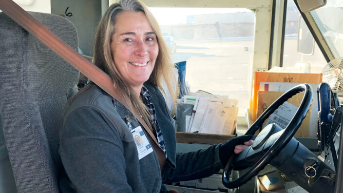 Smiling postal worker sits in delivery vehicle