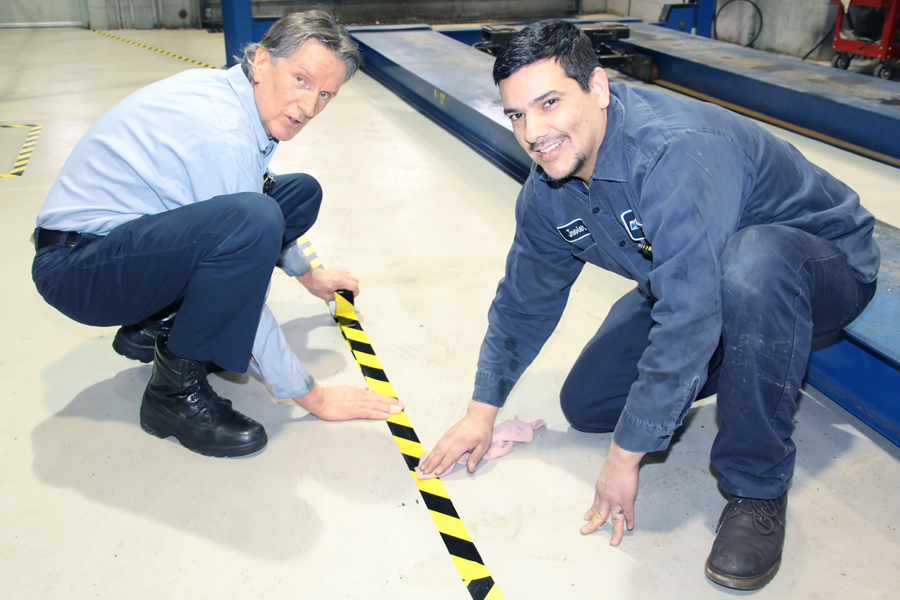 Two smiling men place tape on garage floor