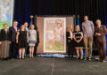 People stand on stage near stamp poster