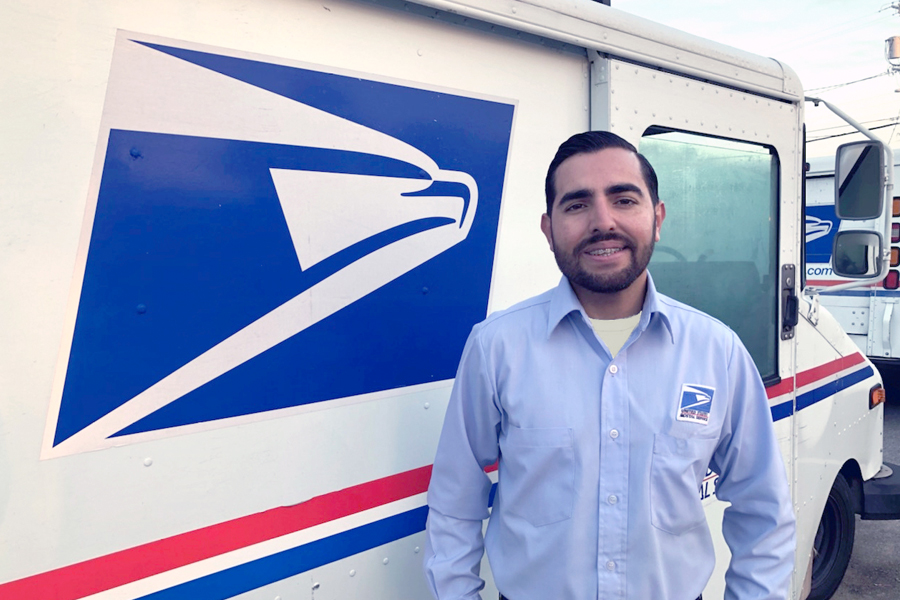 Smiling letter carrier stands next to delivery vehicle