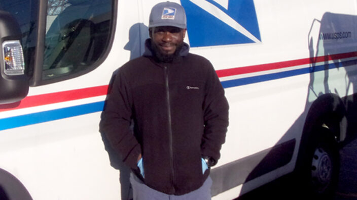 Postal worker stands next to delivery vehicle