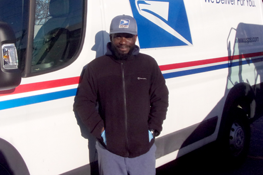 Postal worker stands next to delivery vehicle