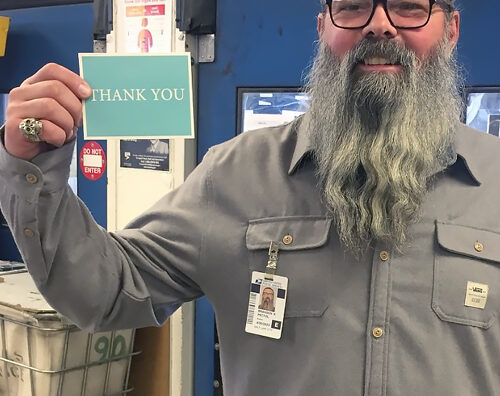 Smiling man stands in postal workroom, holding thank-you card