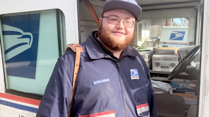 Smiling postal worker stands next to delivery vehicle