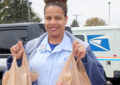 Smiling letter carrier holds two bags of food