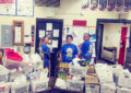 Three people stand inside postal workroom near big carts filled with food