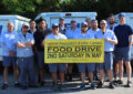 Large group of uniformed postal workers hold banner with food drive information