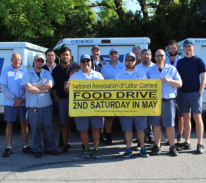 Large group of uniformed postal workers hold banner with food drive information
