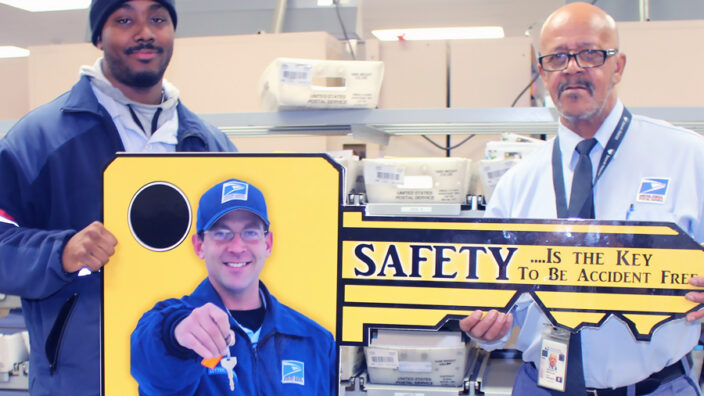 Two smiling men display key-shaped poster with safety slogan