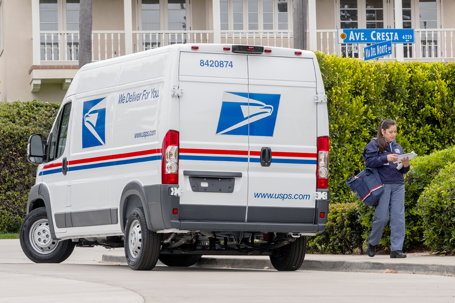 Letter carrier walks near parked USPS delivery vehicle