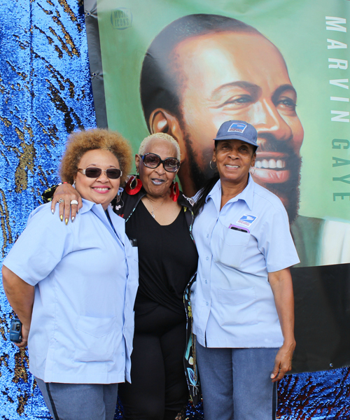 Smiling woman is flanked by two uniformed postal workers