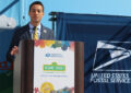 Man in business suit speaks at podium in front of curtain bearing USPS logo