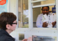 Smiling postal worker shows stamp sheets to customers