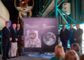 People stand near stamp artwork on stage