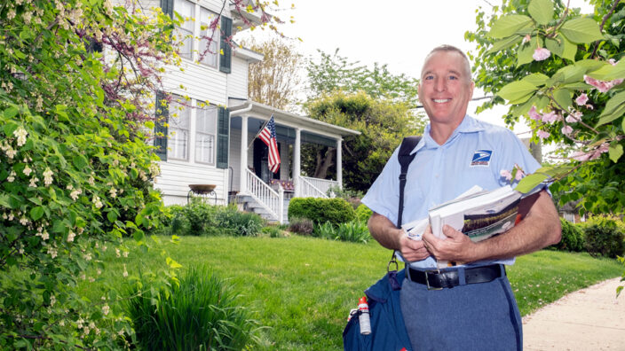 Letter carrier holds mail near house.